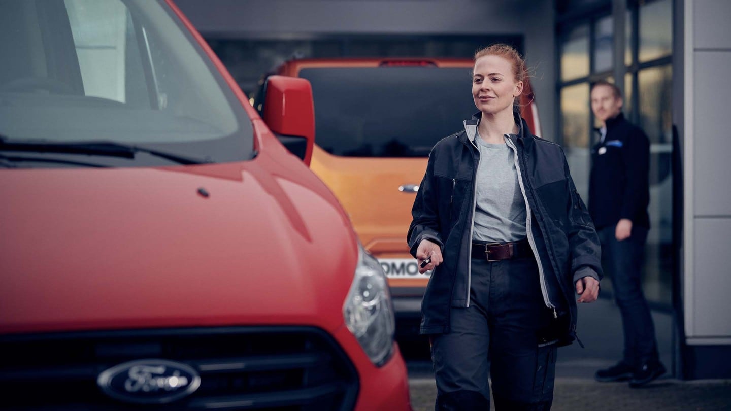 Ford Transit Center Mitarbeiterin geht mit Schlüssel in der Hand auf Ford Transit Custom zu