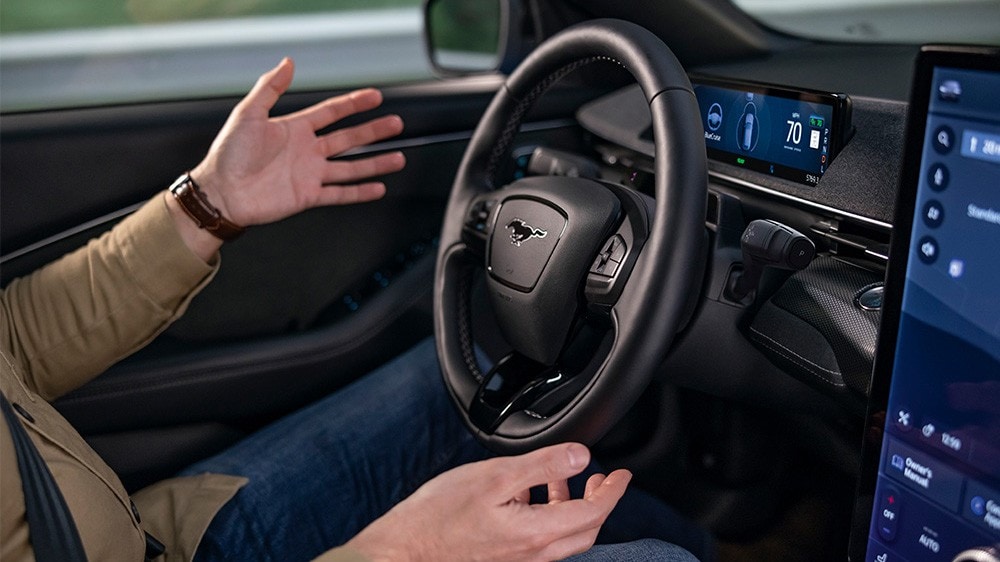 Ein Mann sitzt im Ford Mustang Mach-E, die Hände vom Lenkrad genommen, und demonstriert die BlueCruise-Technologie.