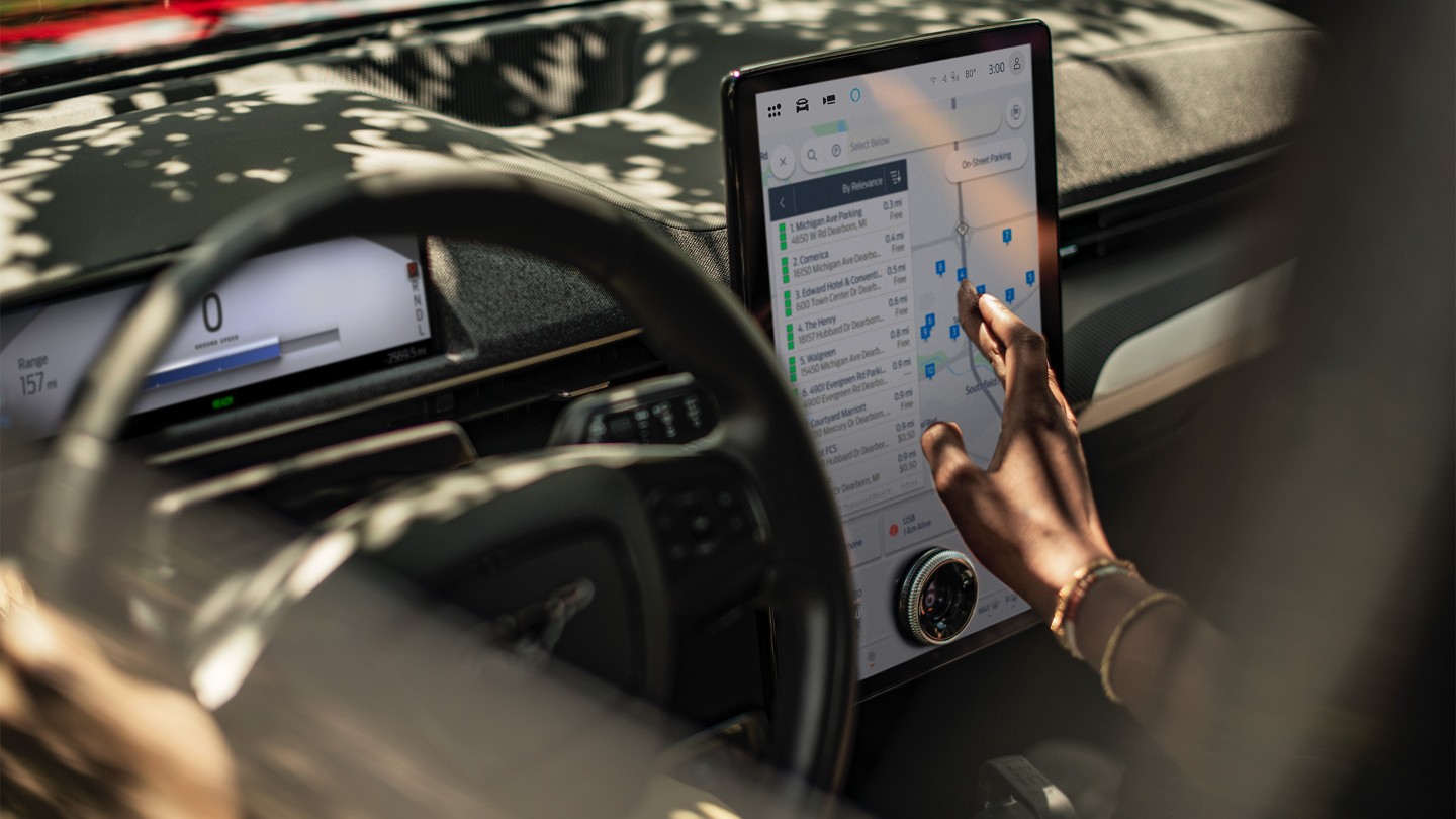 Nahaufnahme einer Frau in einem Ford Mustang Mach-E, die mit dem großen SYNC-Touchscreen interagiert.