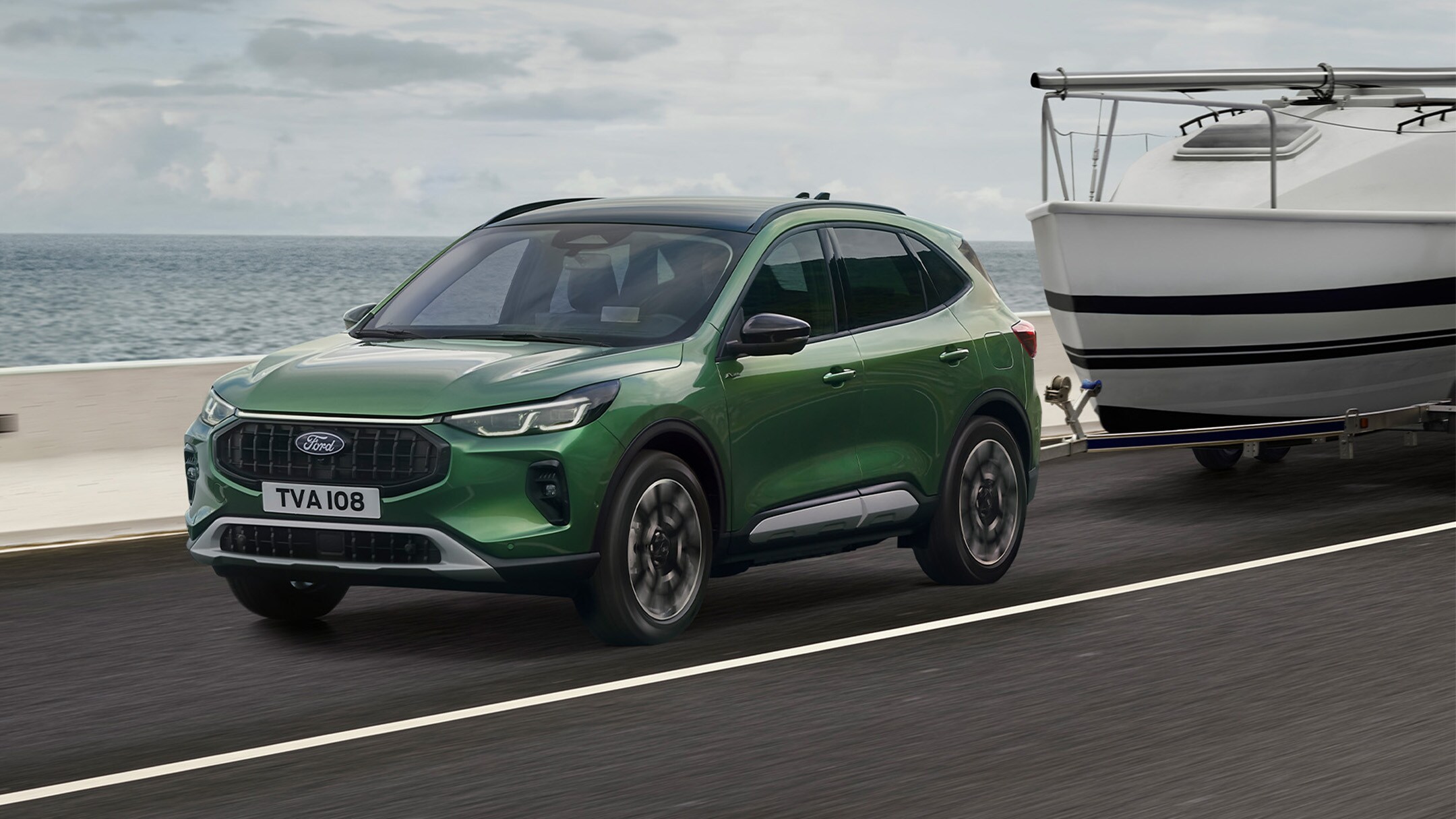 Ein grüner Ford Kuga, der ein kleines Boot entlang einer Küstenstraße zieht.