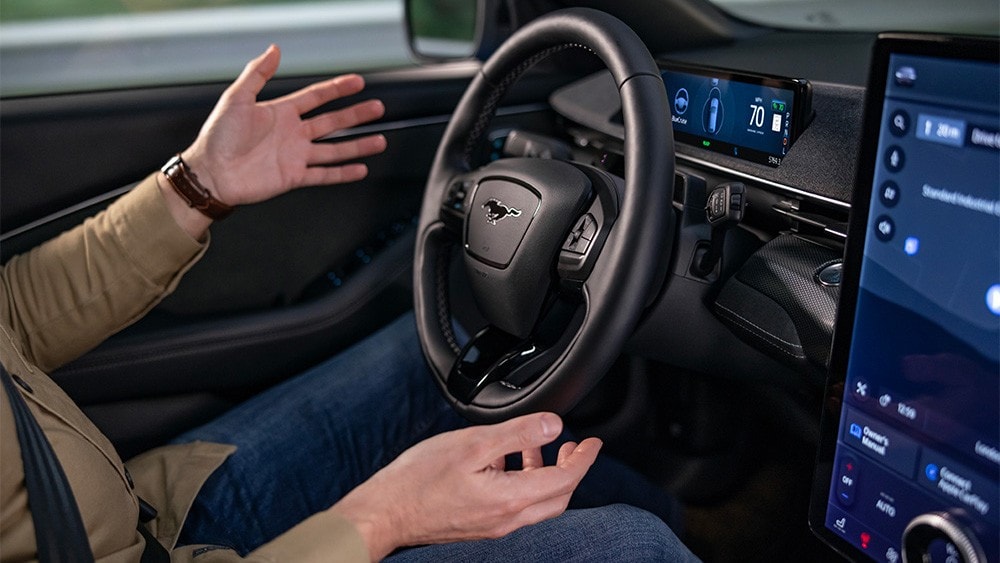 Ein Mann sitzt im Ford Mustang Mach-E, die Hände vom Lenkrad genommen, und demonstriert die BlueCruise-Technologie.