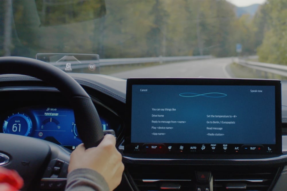 Sicht über die Schulter der Fahrerin durch die Frontscheibe eines Ford Focus auf eine Landstraße