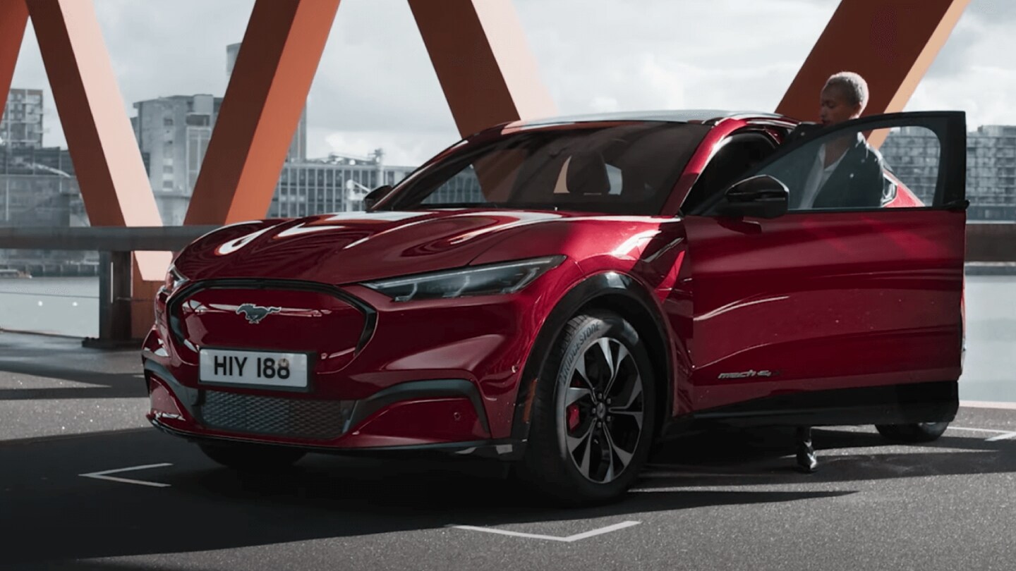 Ford Mach-E in Rot in der ¾-Frontansicht auf einem Parkplatz mit geöffneter Fahrertür