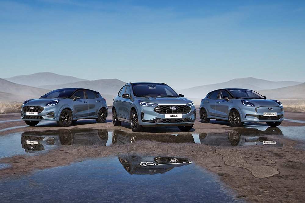 Ein Ford Puma, ein Ford Kuga und ein Ford Puma Gen-E parken auf einer nassen Straße mit Bergen im Hintergrund.