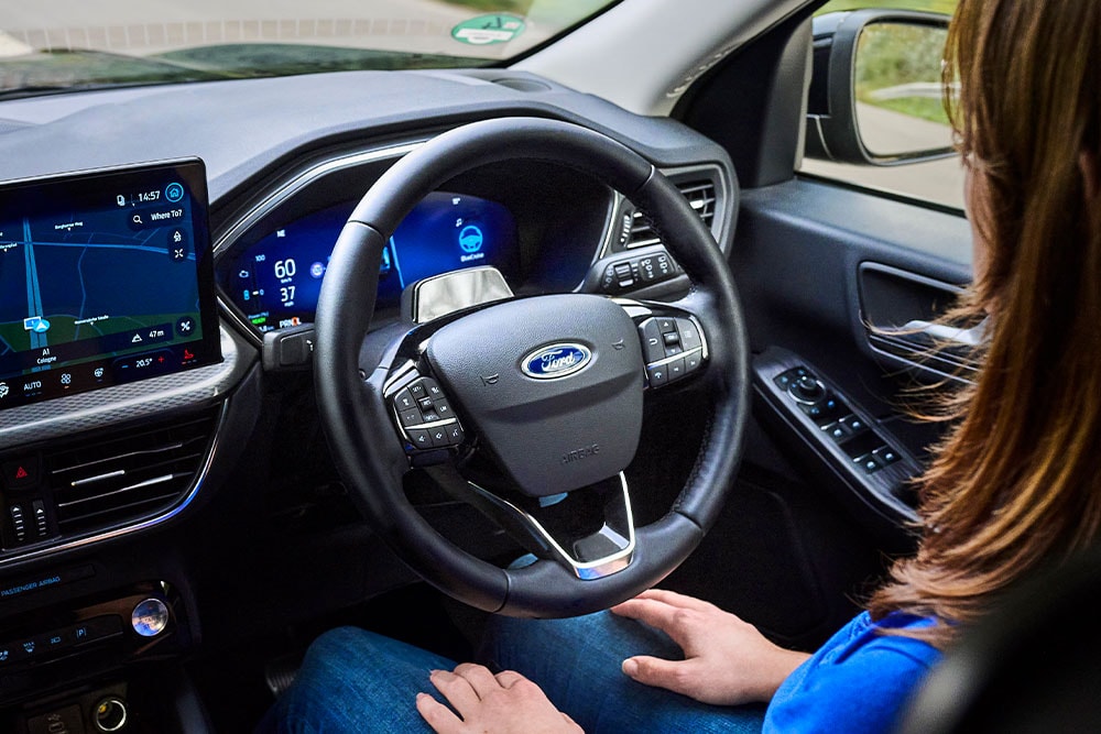 Eine Frau auf dem Fahrersitz eines Ford Kuga, der mit Ford BlueCruise ausgestattet ist, nimmt die Hände vom Lenkrad.