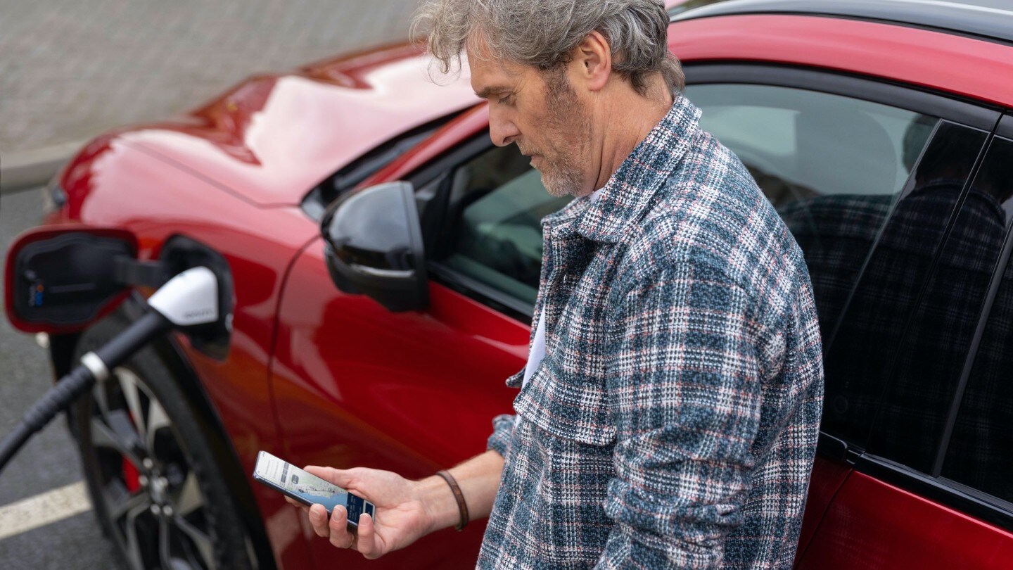 Ein Mann schaut auf sein Smartphone, während er ein Auto auflädt