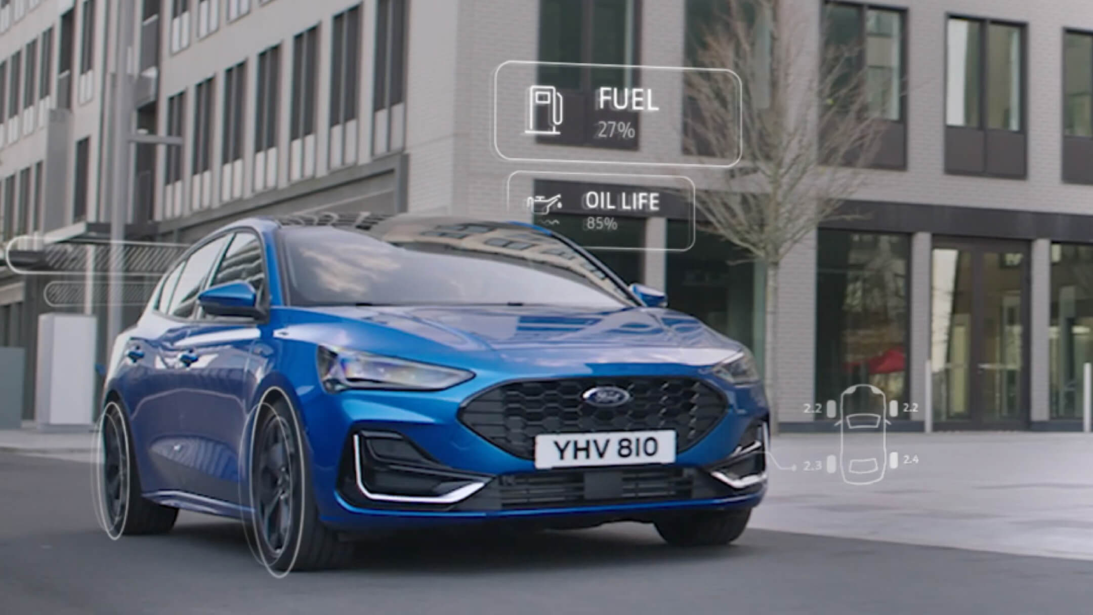 Ford Focus in Blau in der ¾-Frontansicht fährt durch Stadt mit animierten Anzeigen zum Fahrzeugzustand 