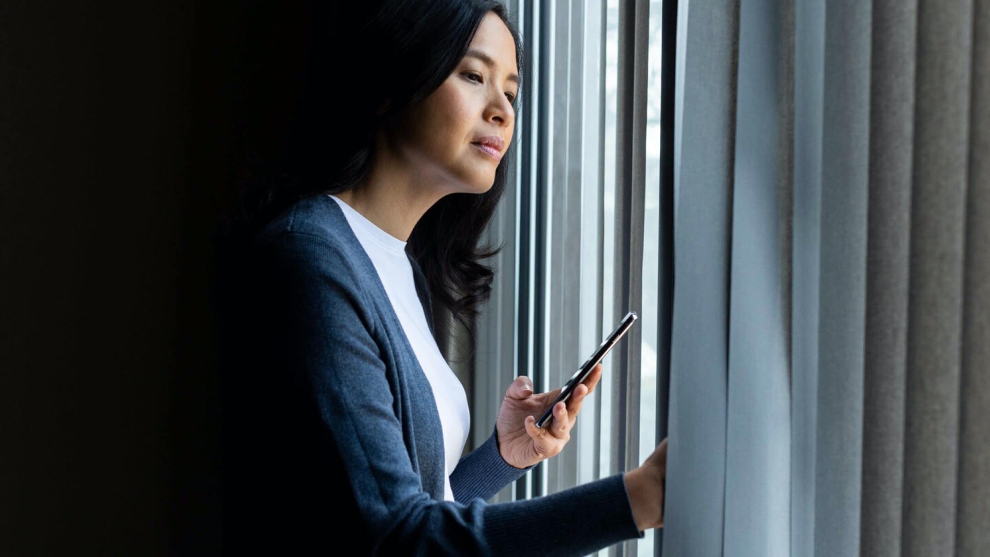 Eine Frau hält ein Smartphone und schaut aus dem Fenster