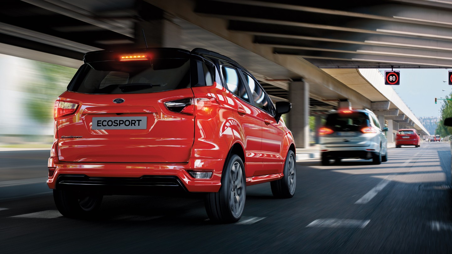 Ford Ecosport in Rot. Dreiviertelansicht von hinten. Fahrszene unter einer Brücke