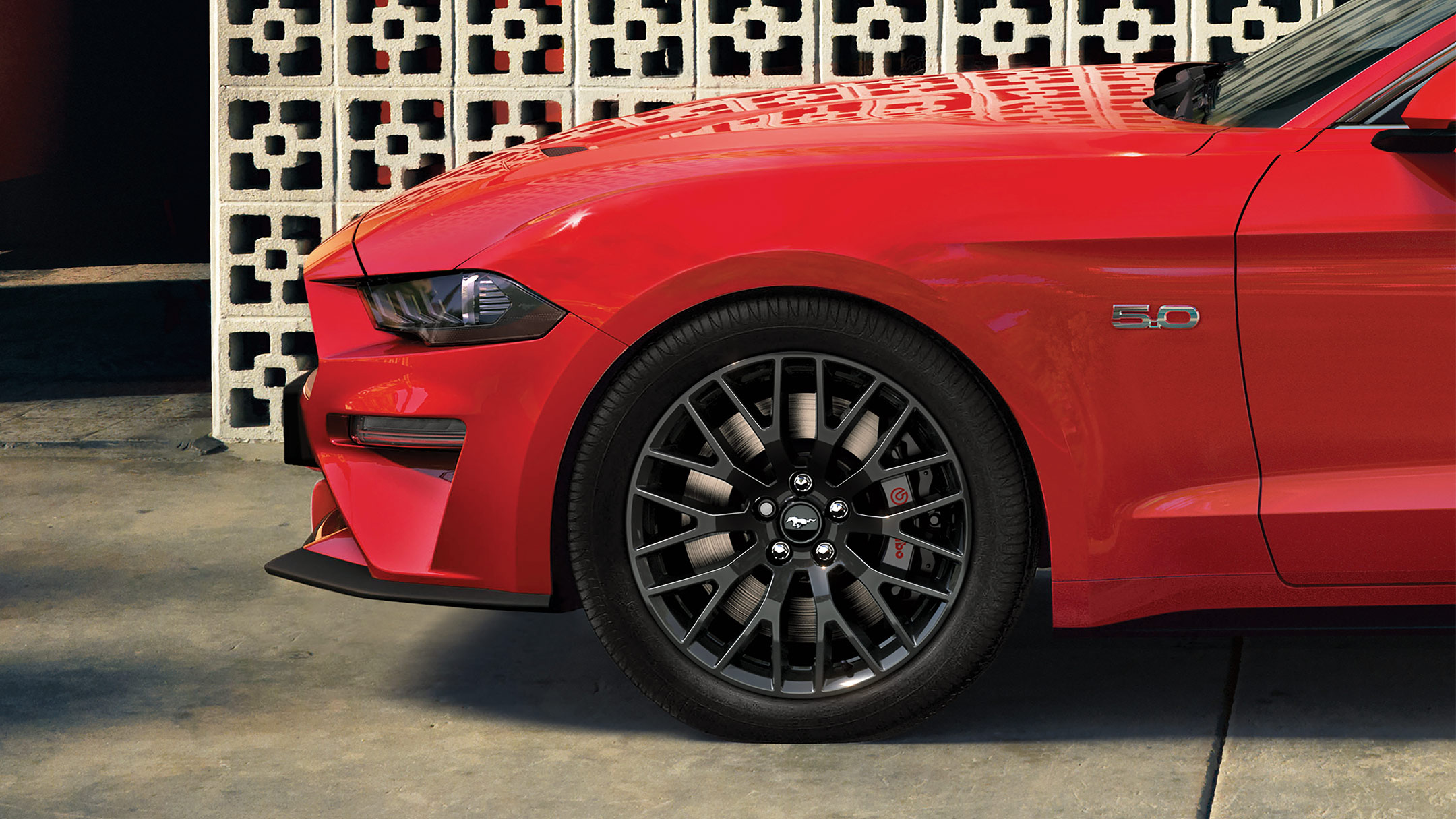  Ford Mustang in Rot. Seitenansicht der Front, parkend vor einer verzierten Steinmauer