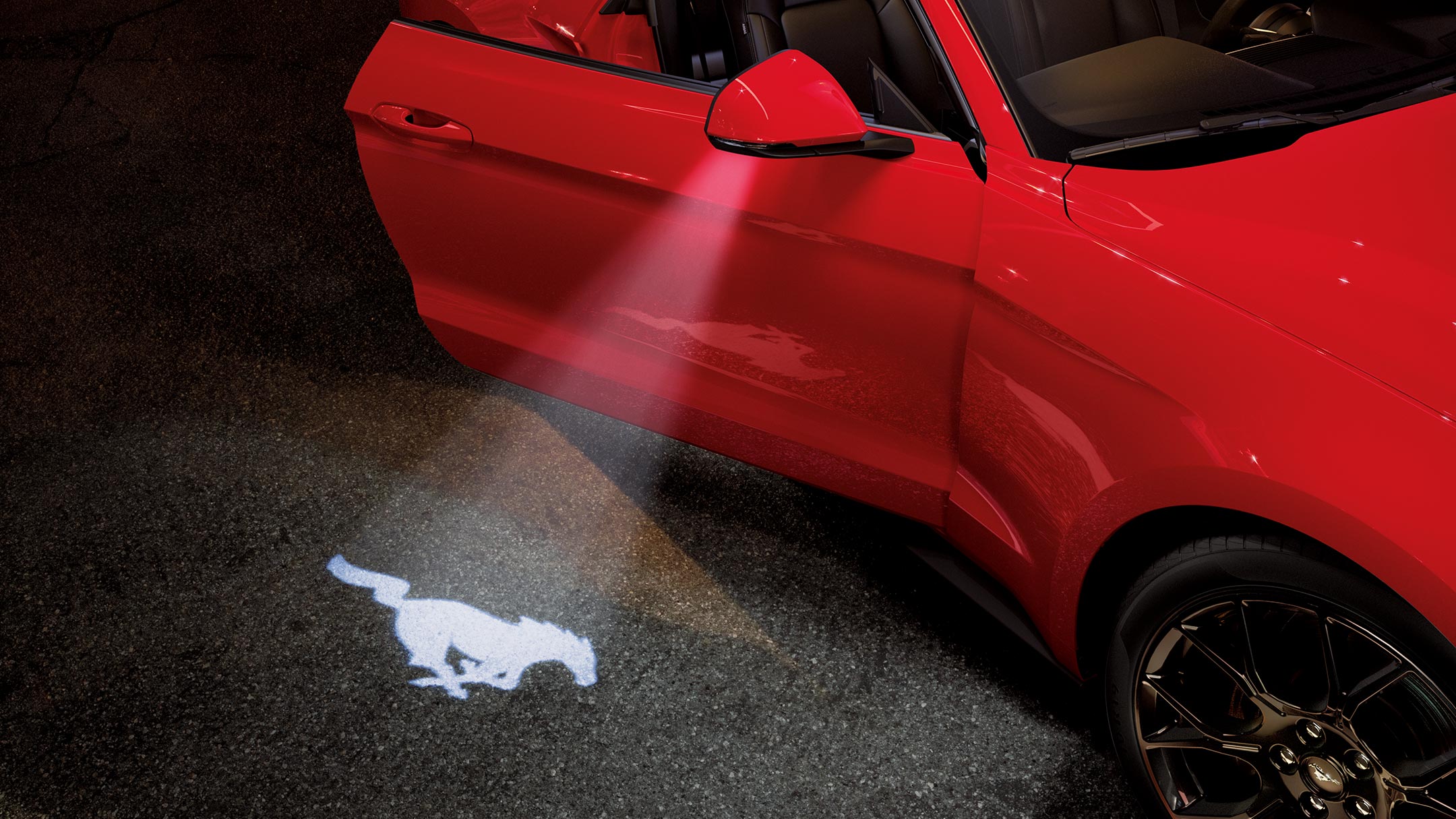 Ford Mustang in Rot. Dreiviertelansicht, parkend mit geöffneter Tür und Mustang-Pony-Form-Lichtkegel