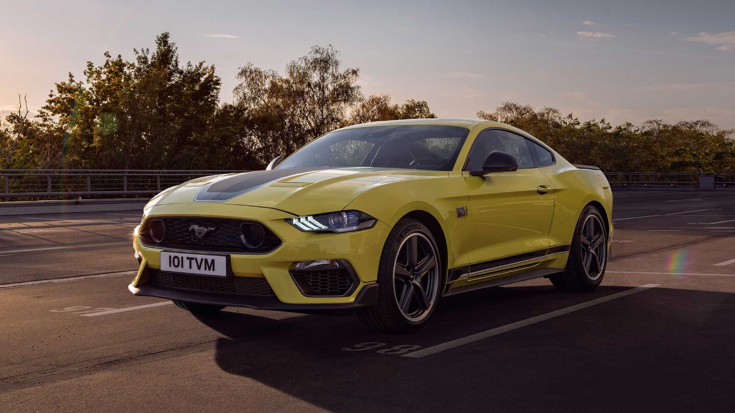 Ford Mustang in Gelb in der 3/4 Frontansicht bei Sonnenuntergang auf einer  mehrspurigen Straße fahrend 