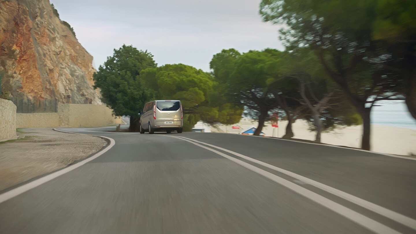 Ford Tourneo Custom Champagner Heckansicht in Bewegung auf Uferstraße 