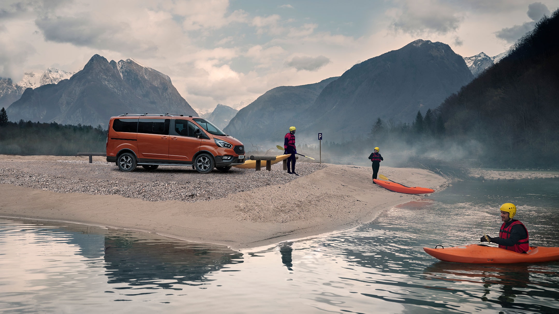 Ford Tourneo Custom Active Orange Seitenansicht parkt im Gebirge an steinigem Fluss mit Paddlern und Booten