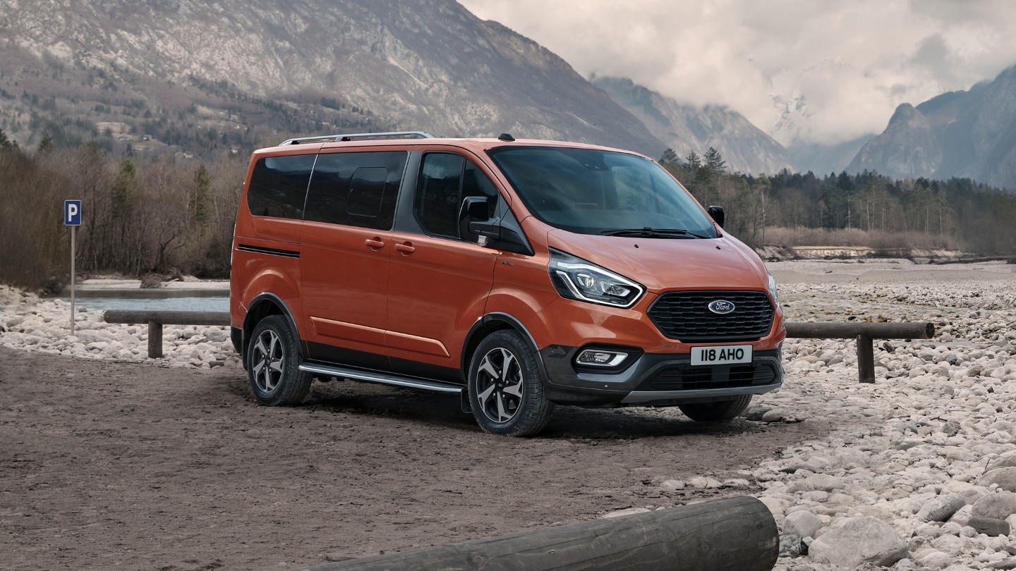 Ford Tourneo Custom Active Orange ¾-Frontansicht parkt neben Flussbett im Gebirge 