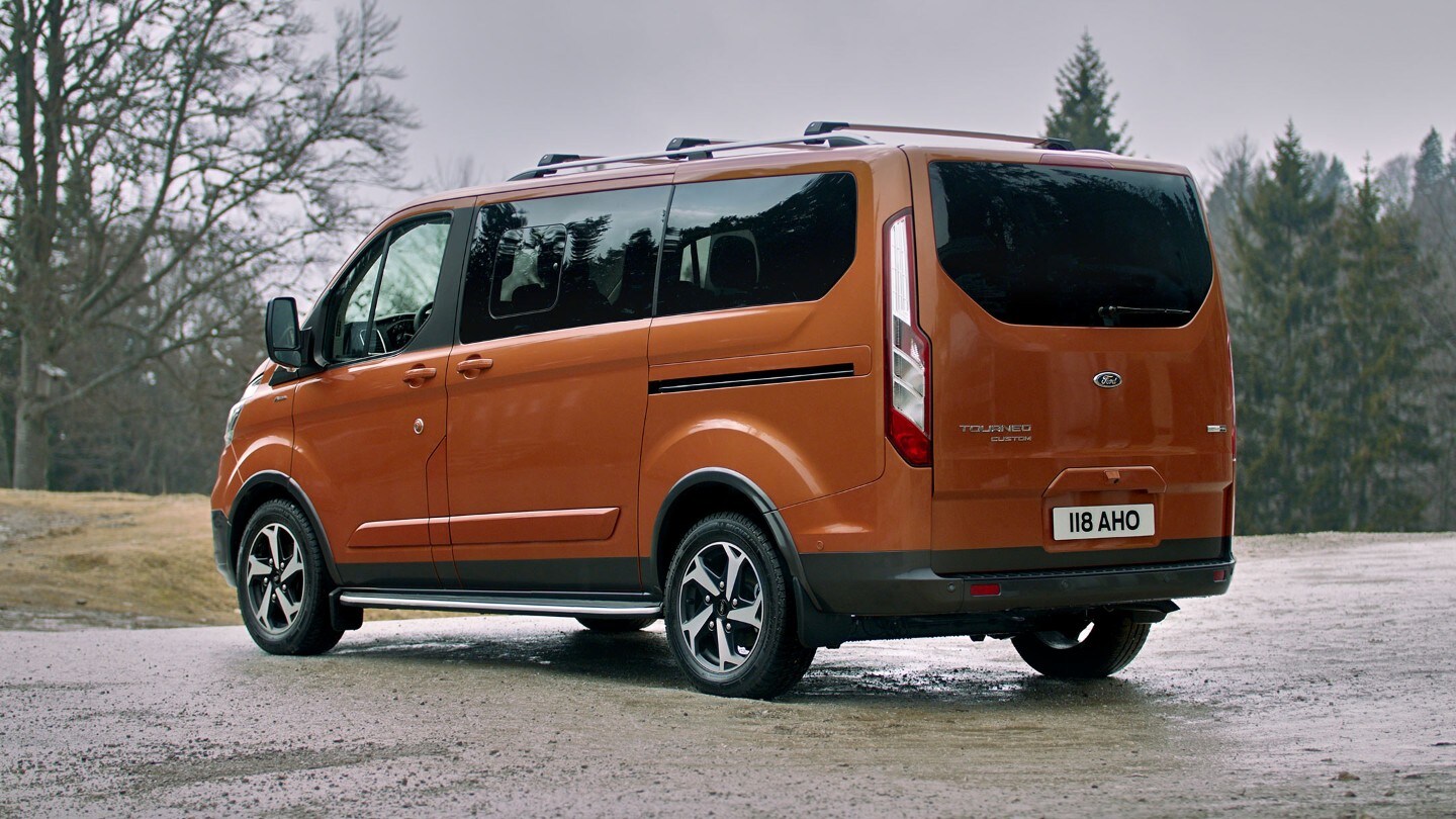 Ford Tourneo Custom Active Orange ¾-Heckansicht parkt auf Waldparkplatz 