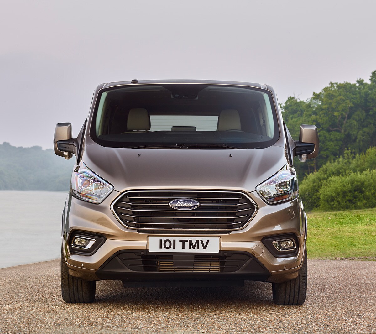 Ford Tourneo  Custom Champagner Frontansicht parkt vor Gewässer und Wiese