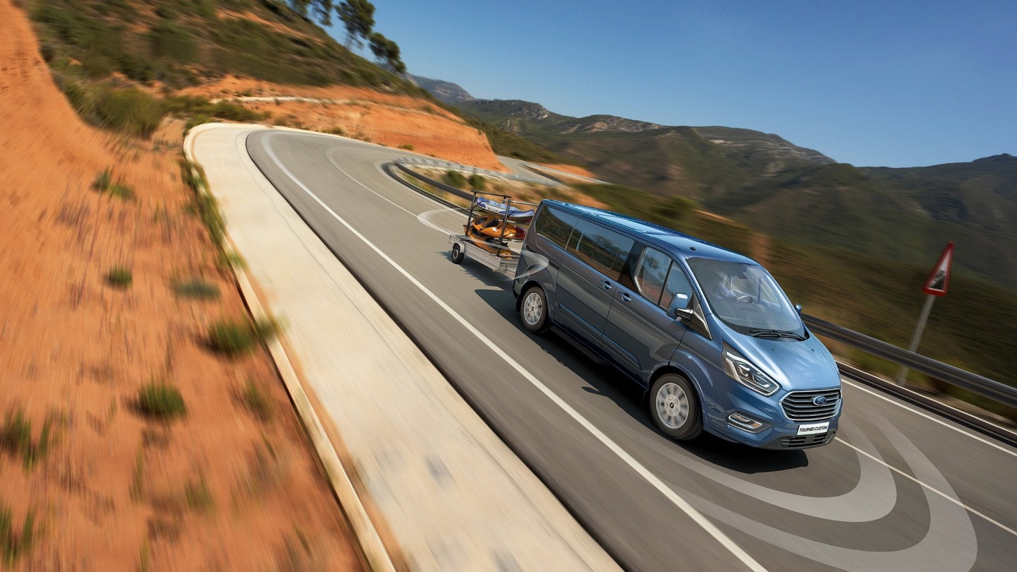 Ford Tourneo Custom Blau mit Anhänger bergab in Bewegung 