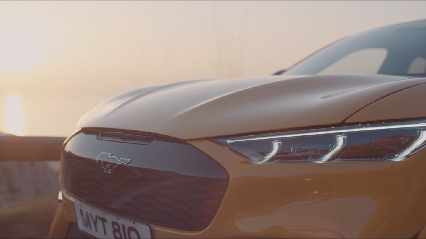 Ford Mustang Mach-E in Gelb. Heckansicht. Fahrend auf einer Landstraße beim Dämmerung