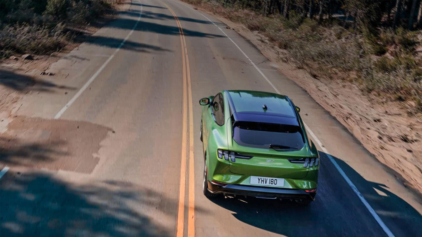 Ein grüner Ford Mustang Mach-E GT  fährt auf einer von Bäumen gesäumten Bergstraße.