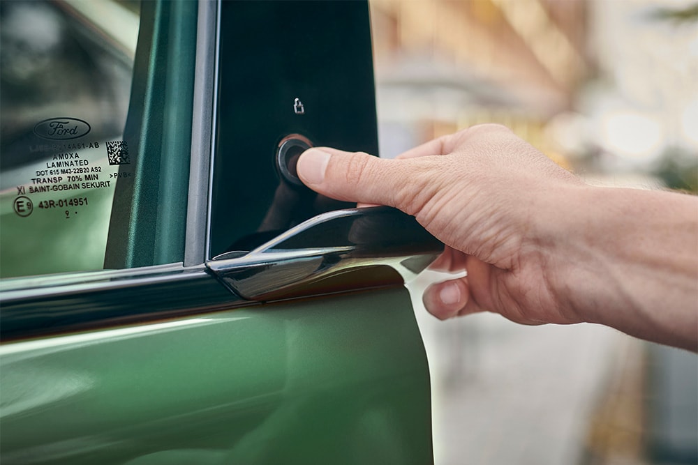 Hand, die  durch Drücken eines Knopfes an der Tür eines grünen Ford Mustang Mach-E die Tür öffnet.