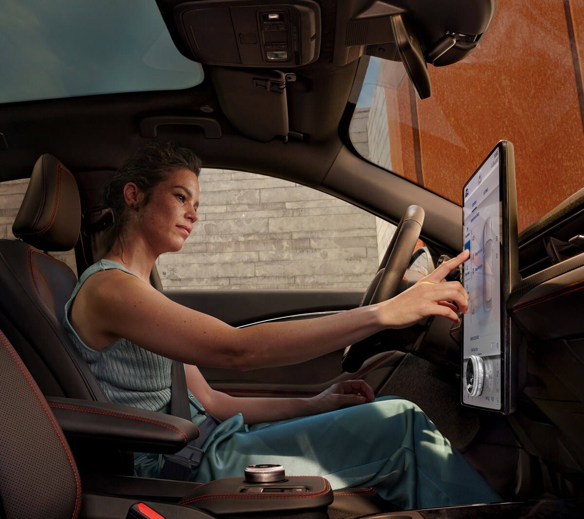 Ford Mustang Mach-E. Innenraumansicht. Fahrerin benutzt Ford SYNC 4A Touchscreen