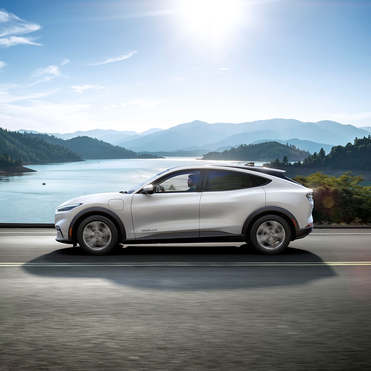 Ford Mustang Mach-E in Silber Seitenansicht fahrend vor See