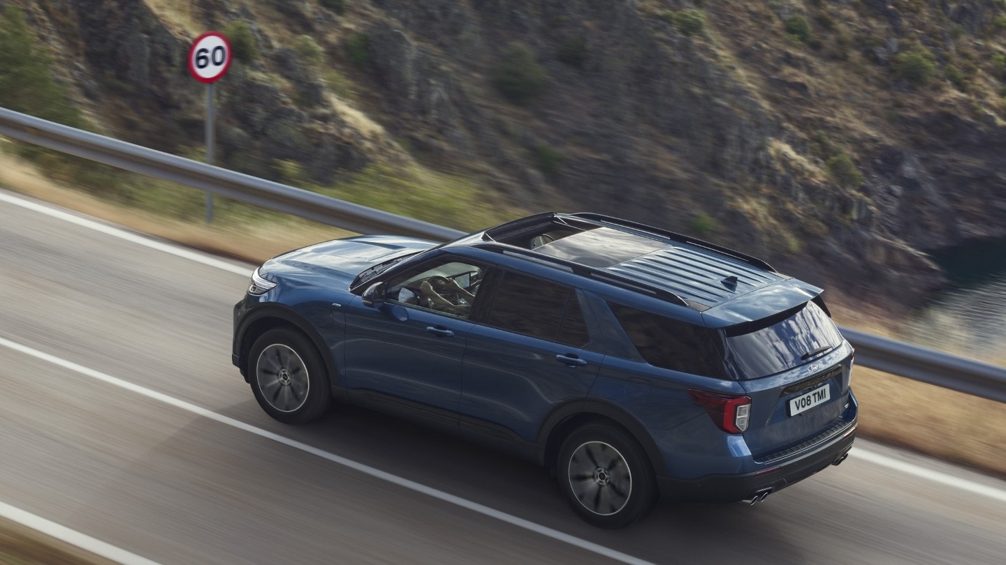 Ford Explorer Plug-in-Hybrid in Blau. Dreiviertel-Heckansicht. Eine Straße in den Bergen bergauf fahrend