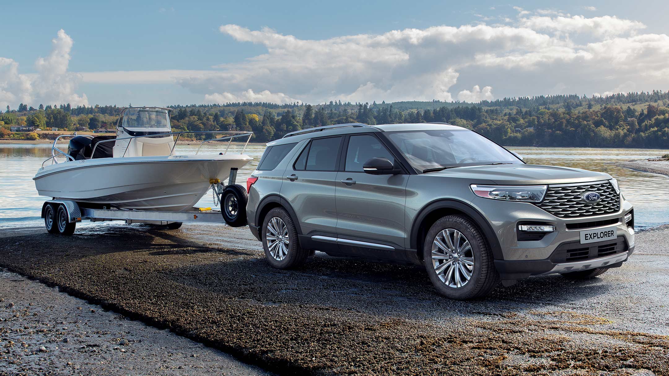 Ford Explorer Plug-in-Hybrid in Silber. Dreiviertel-Frontansicht. Mit Bootsanhänger an einem See