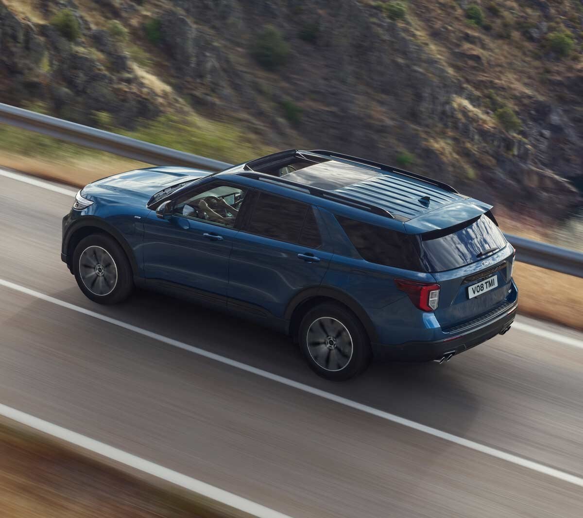 Ford Explorer Plug-in-Hybrid in Blau. Dreiviertel-Heckansicht. Eine Straße in den Bergen bergauf fahrend