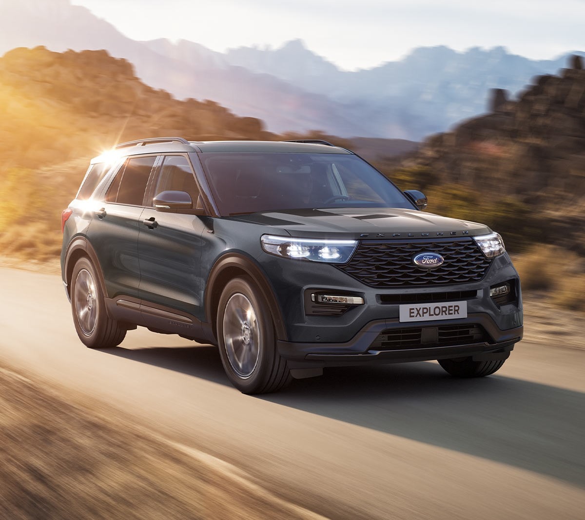 Ford Explorer Plug-in-Hybrid in Blau. Dreiviertel-Frontansicht. Fahrszene auf einer Landstraße mit Bergen im Hintergrund