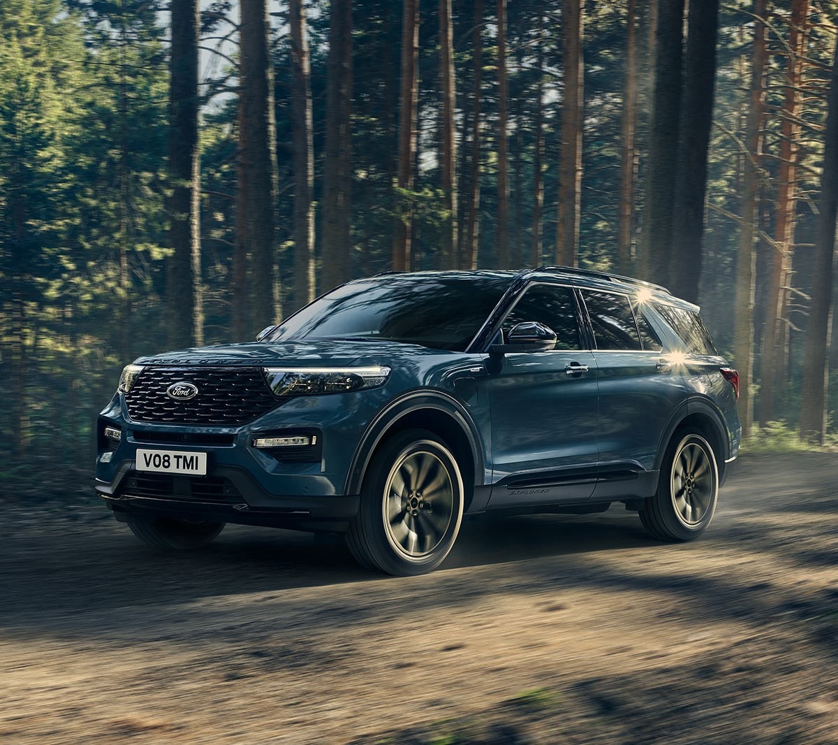 Ford Explorer Plug-in-Hybrid in Blau. Dreiviertel-Frontansicht. Fahrszene auf einer Landstraße mit Wald im Hintergrund