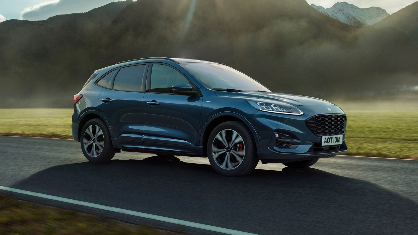 Ford Kuga in Blau. 3/4-Frontansicht, fahrend auf einer Landstraße mit Bergen im Hintergrund