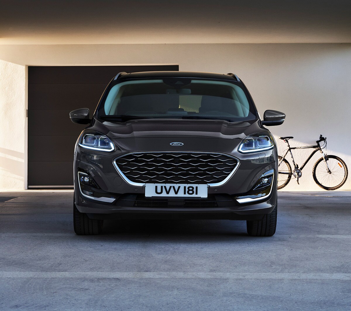 Ford Kuga in Blau. Frontansicht, vor einer Garage unter dem Abdach eines modernen Gebäudes parkend