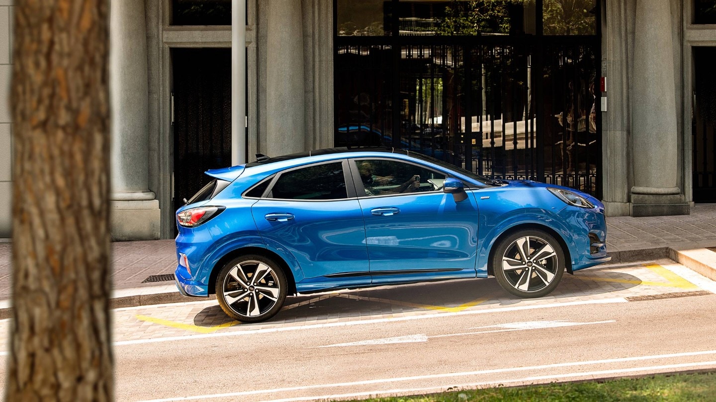 Ford Puma in Blau. Seitenansicht an einer ansteigenden Straße, vor einem Restaurant