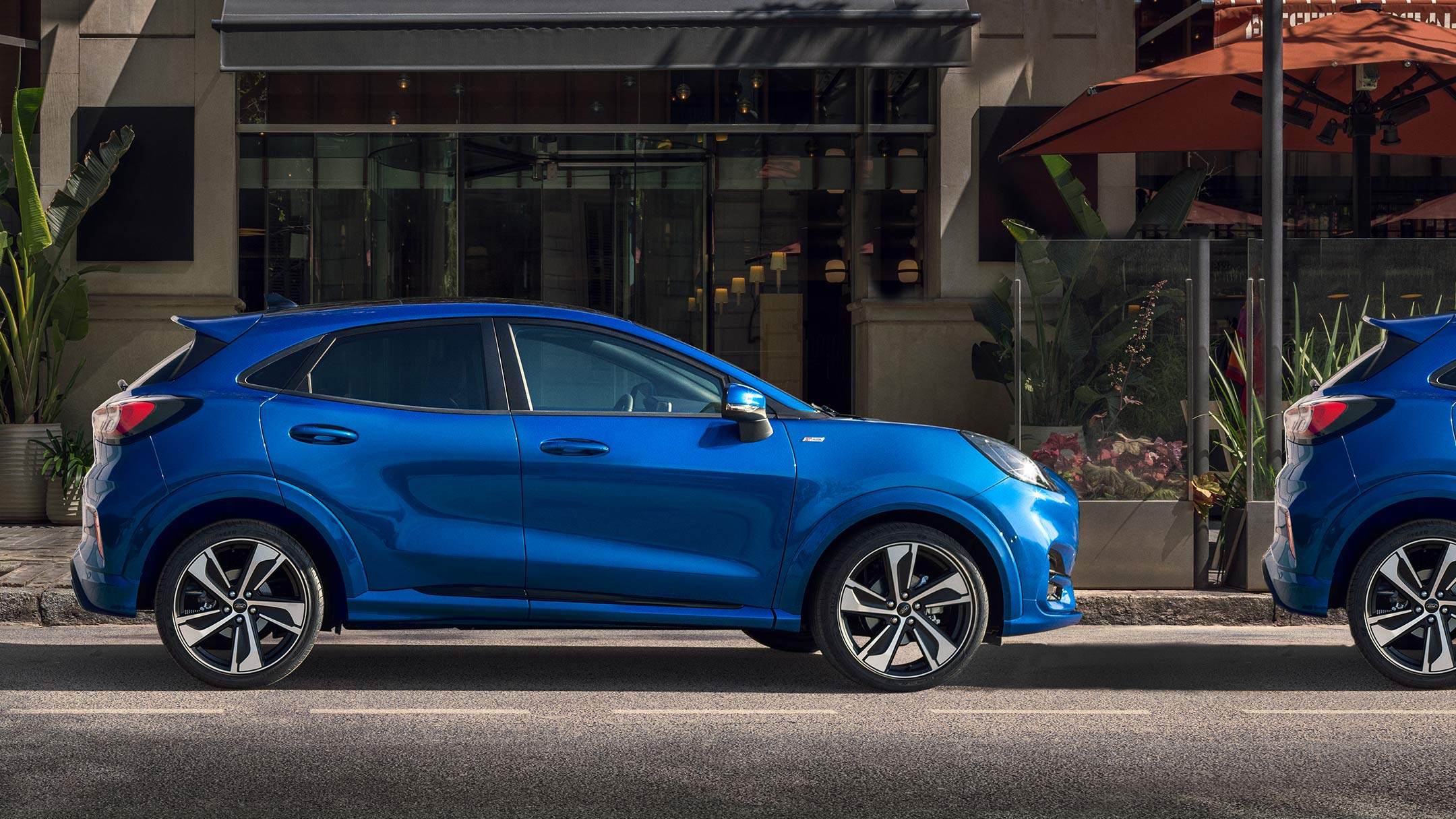 Ford Puma ST-Line X in blau von der Seite in einer Parklücke vor einem Haus.