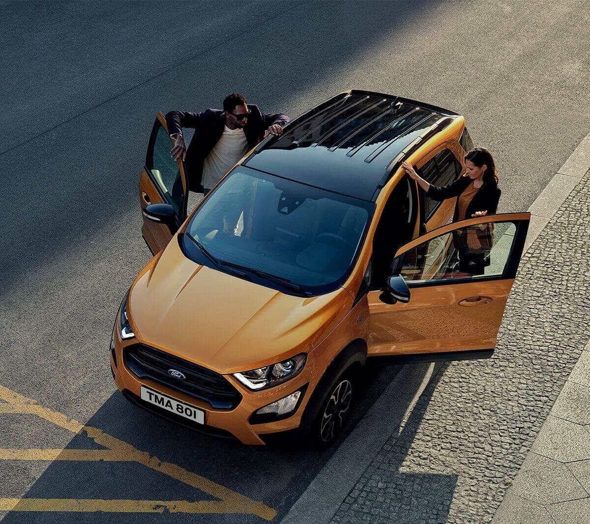 Ford EcoSport Active in Orange. 3/4-Frontansicht von oben. Frau und Mann steigen in das Fahrzeug ein