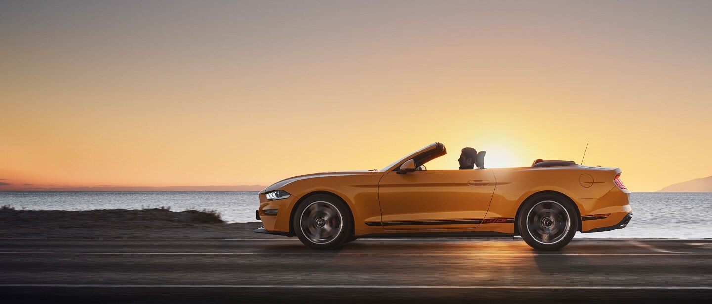 Ford Mustang California in Orange. Seitenansicht, in der Natur im Sonnenuntergang fahrend.