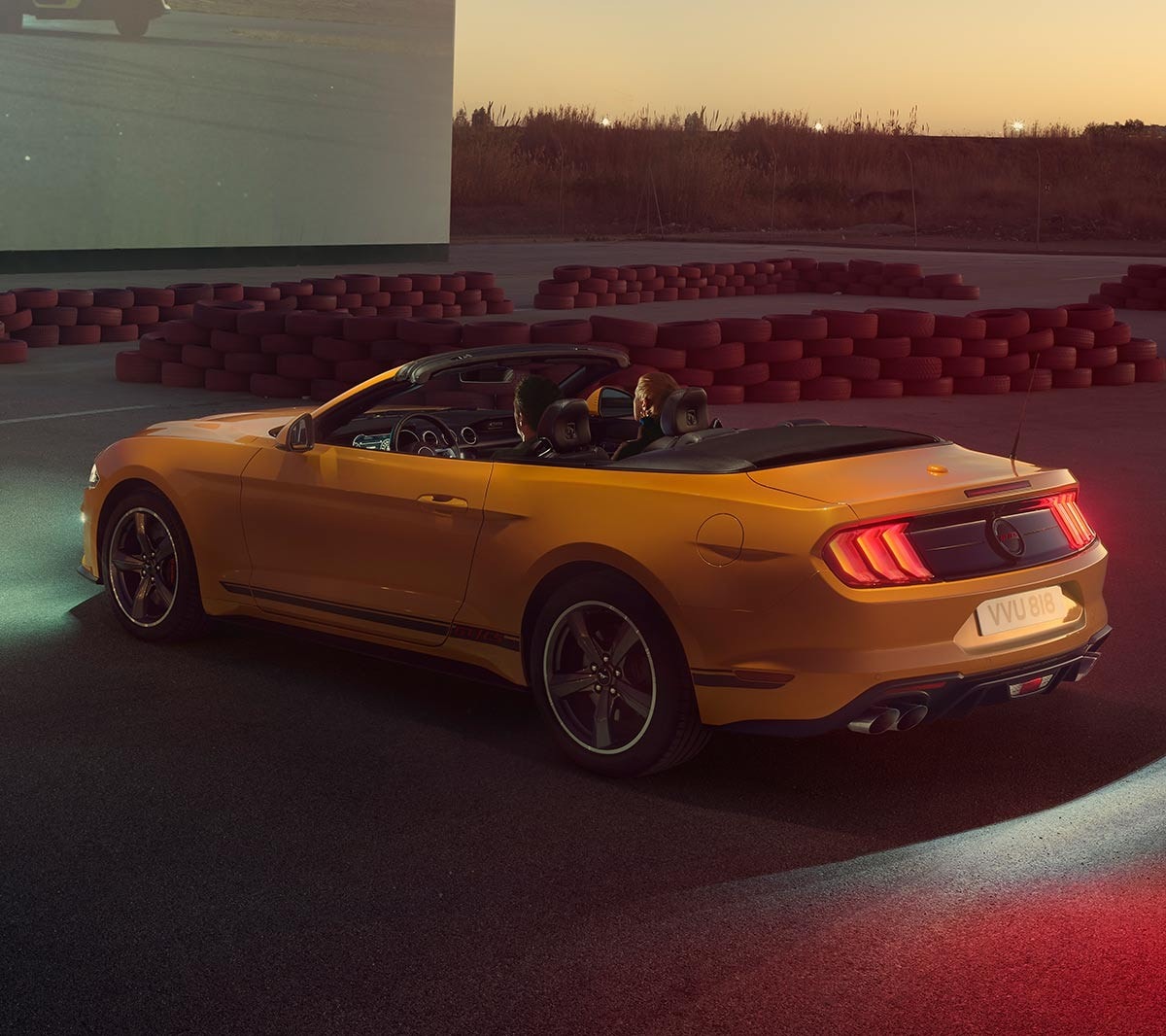 Ford Mustang California in Orange. Dreiviertel-Frontansicht, vor einer Leinwand parkend.