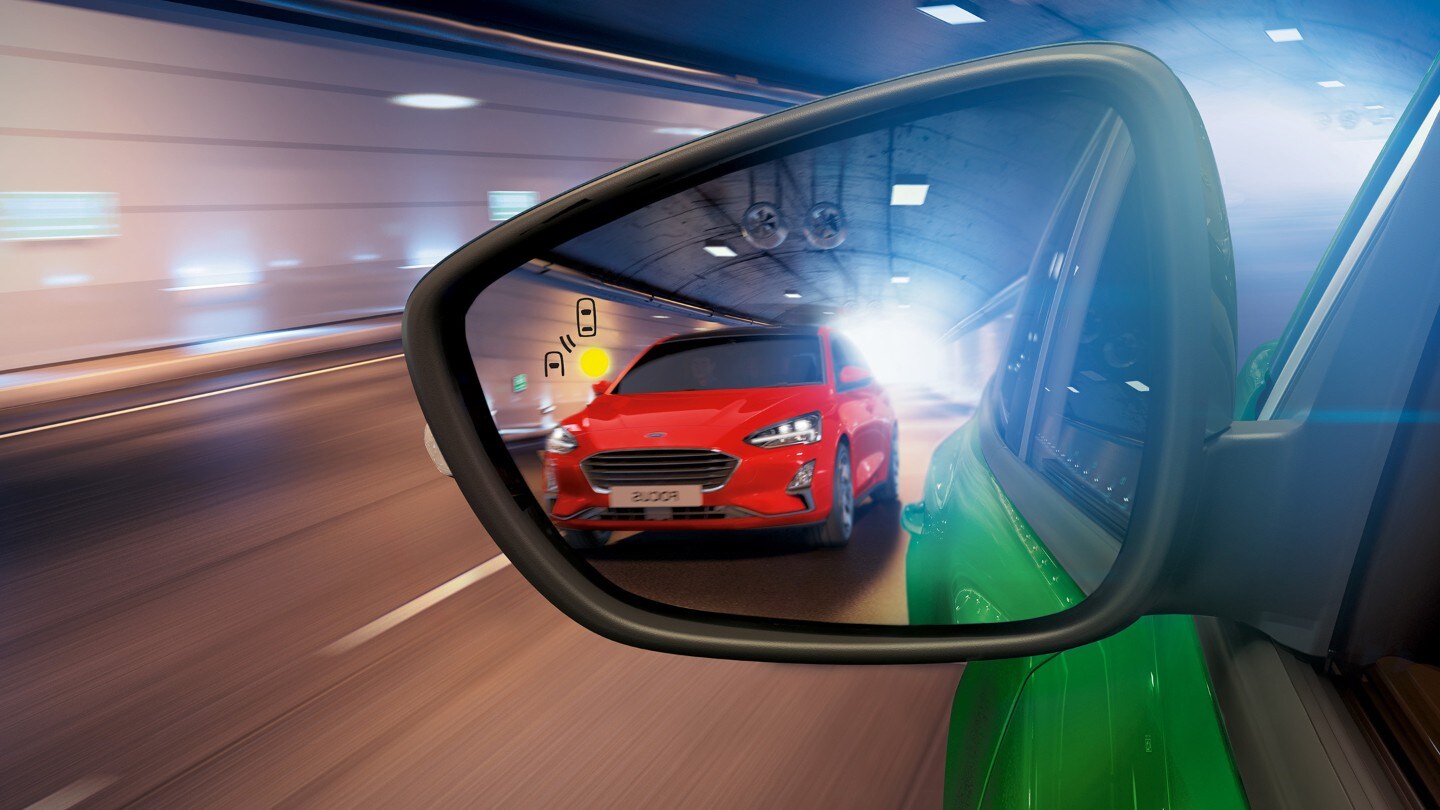 Ford Puma ST in Grün. Detailansicht des Außenspiegels mit rotem Ford Focus im Hintergrund