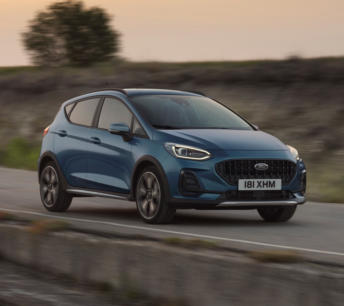 Ford Fiesta in Blau. Dreiviertel-Frontansicht, auf einer Straße im Sonnenuntergang fahrend.