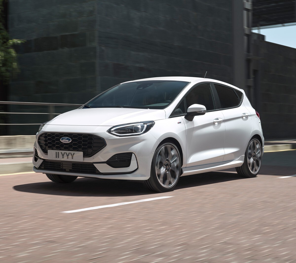 Ford Fiesta in Weiß. Dreiviertel-Frontansicht in einer Stadt fahrend mit modernen Gebäuden im Hintergrund.