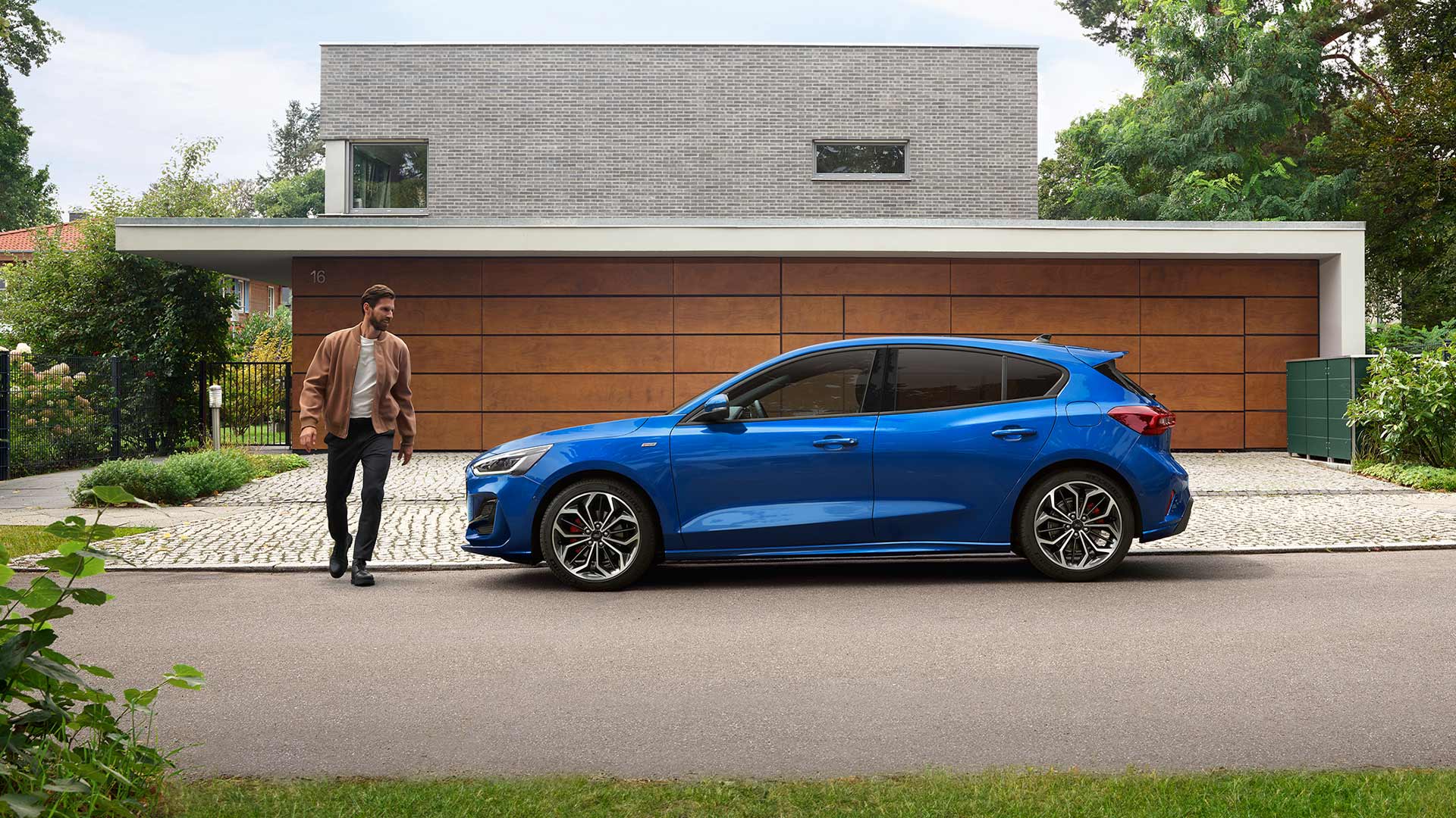 Ein Mann nähert sich einem blauen Ford Focus, der vor einem Haus geparkt ist