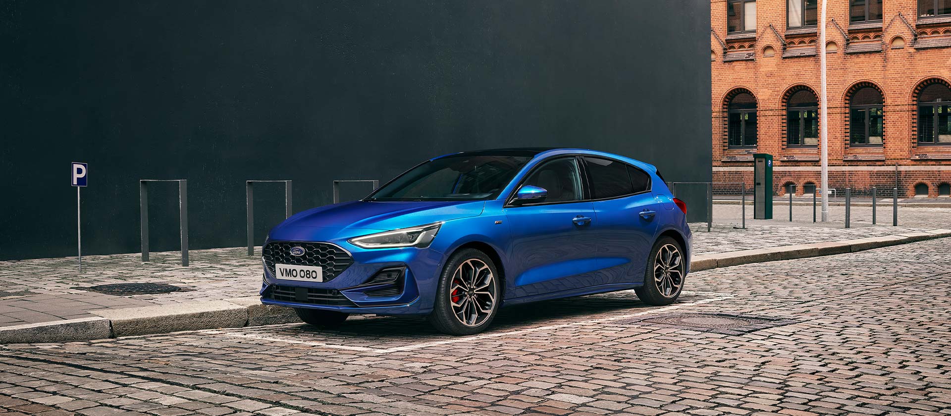 Ein blauer Ford Focus Schrägheck steht auf einer Kopfsteinpflasterstraße in einer städtischen Umgebung.