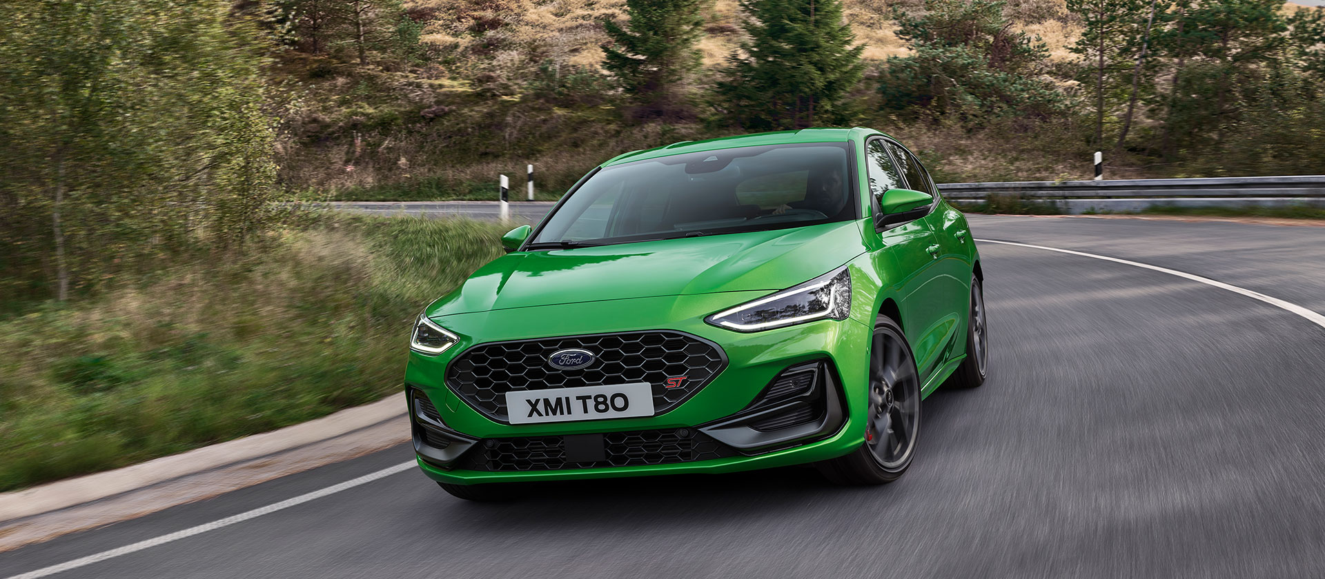 Ein Ford Focus ST in Mean Green fährt auf einer malerischen Straße um eine Kurve.