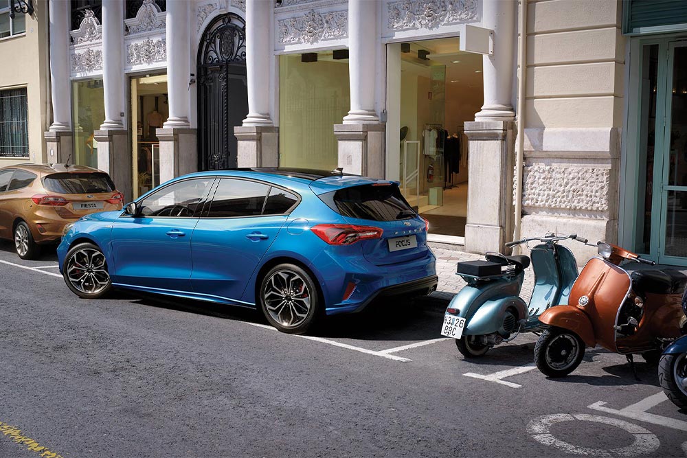 Ein blauer Ford Focus parkt mithilfe des Active Park Assist in einer Parklücke in der Stadt.