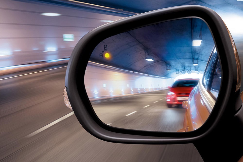 Ein Seitenspiegel in einem Tunnel aus der Fahrerperspektive: Ein rotes Auto nähert sich im toten Winkel.