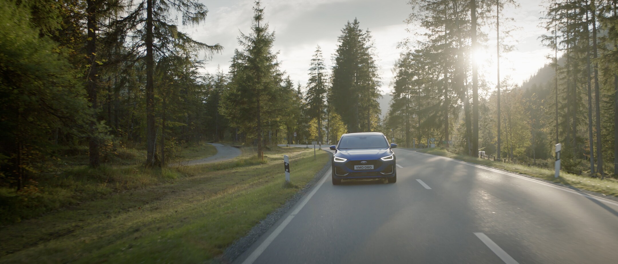 Ford Focus ST-Line in Blau. Seitenansicht, auf einer Straße durch einen Wald fahrend. Ford Focus ST-Line in Blau. Seitenansicht, auf einer Straße durch einen Wald fahrend.