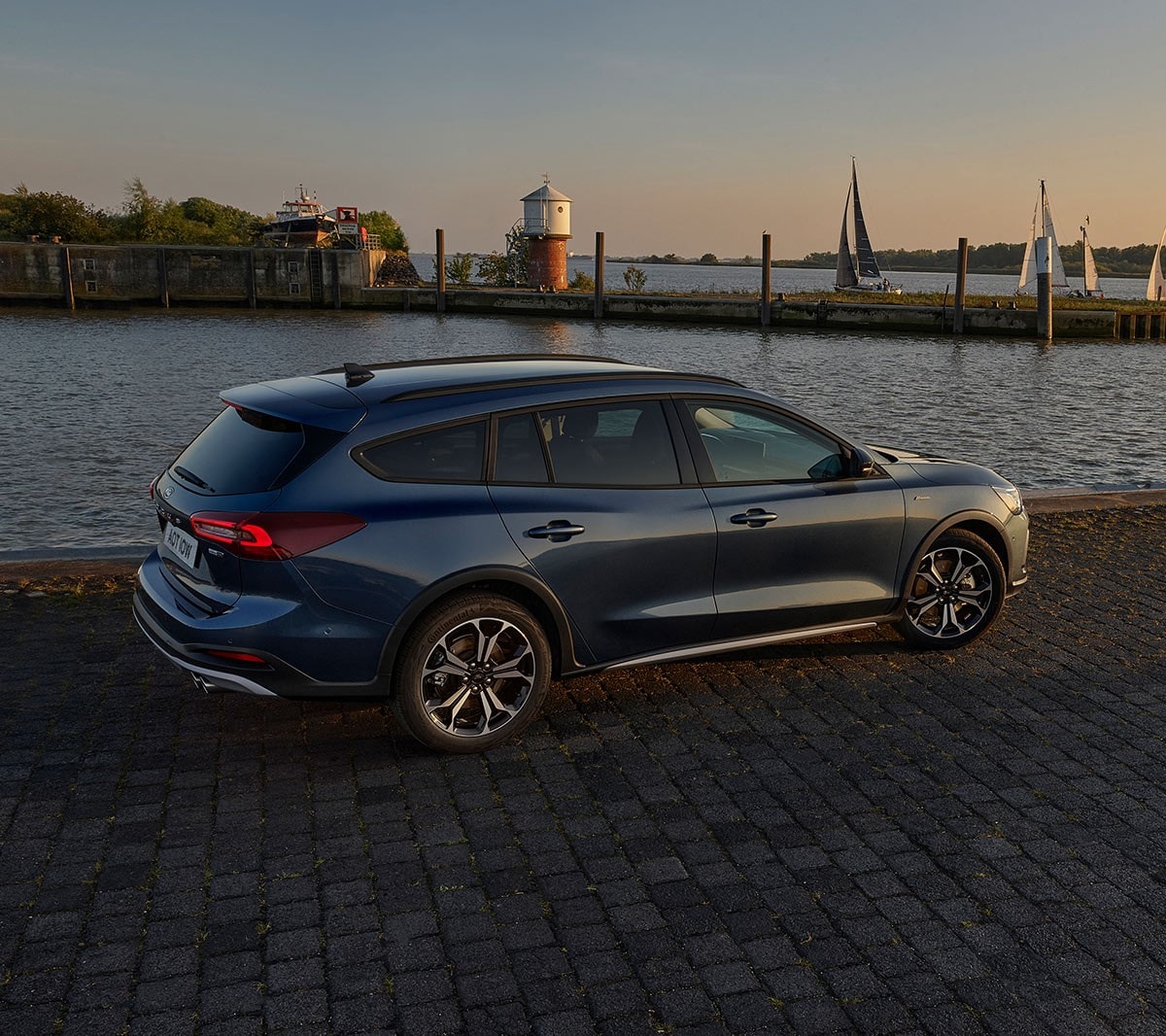 Ford Focus in Blau. Dreiviertel-Heckansicht, vor einem See im Sonnenuntergang parkend.