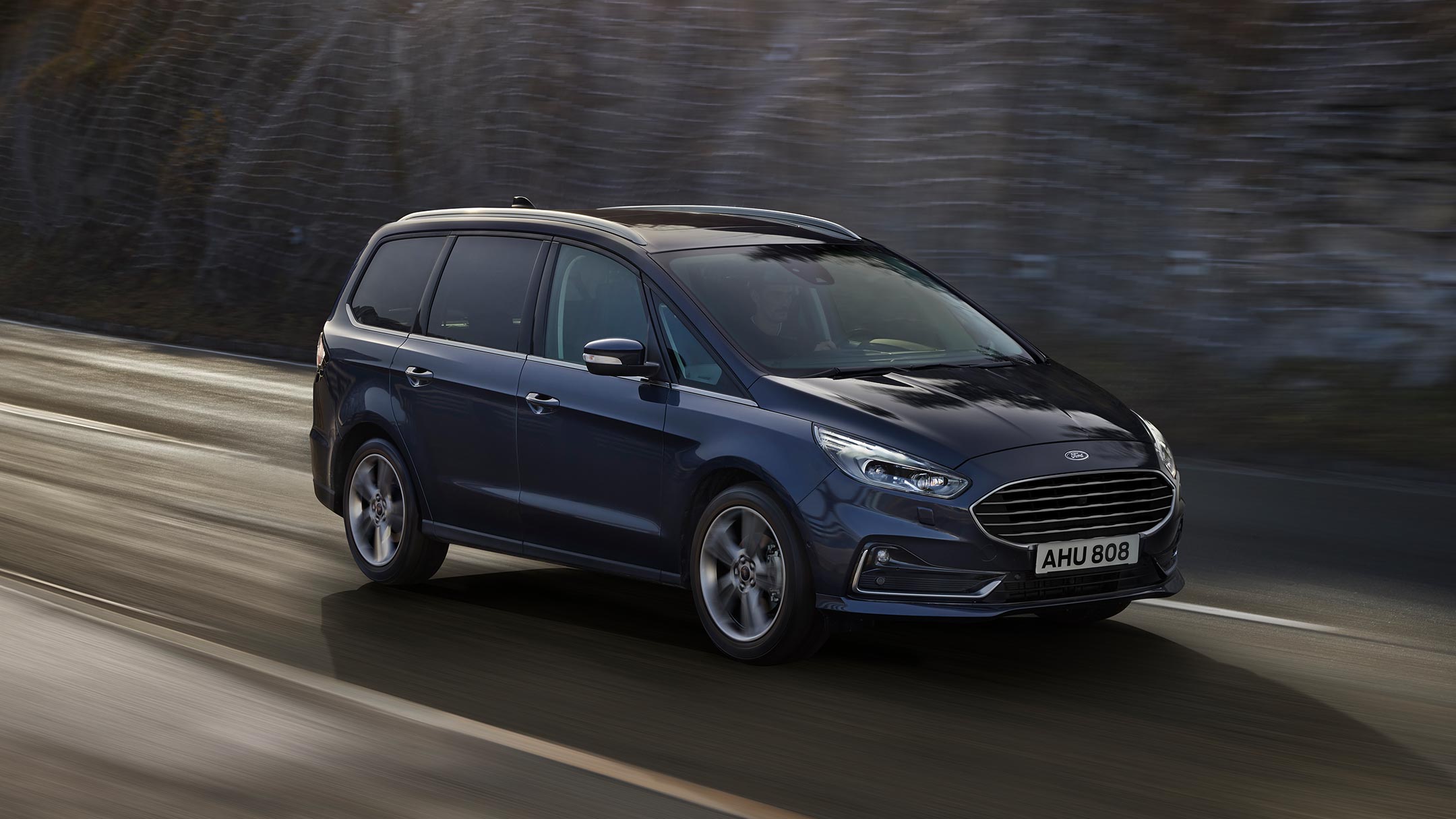 Ford Galaxy Hybrid in Blau. 3/4-Frontansicht. Fahrszene auf einer Bergpanorama-Straße